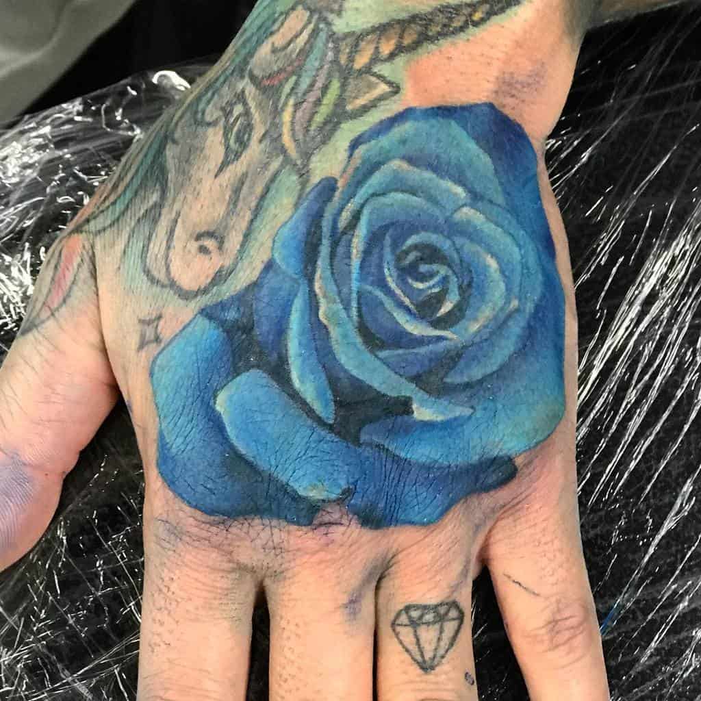 A detailed blue rose tattoo elegantly adorns the back of a hand