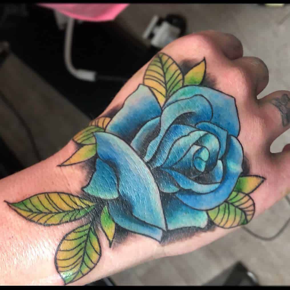 A blue rose tattoo with green leaves on a person's hand