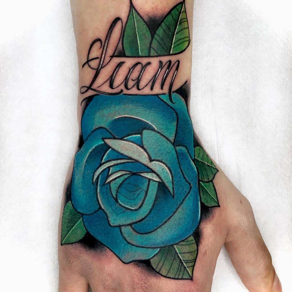 A striking tattoo graces the hand, featuring a blue rose with lush leaves elegantly entwined beneath the name "Liam"