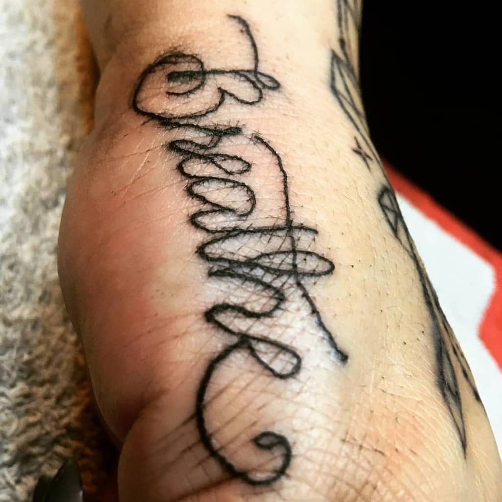 In elegant cursive, the tattoo gently whispers the word "Breathe," offering a constant reminder to inhale deeply and savor each moment