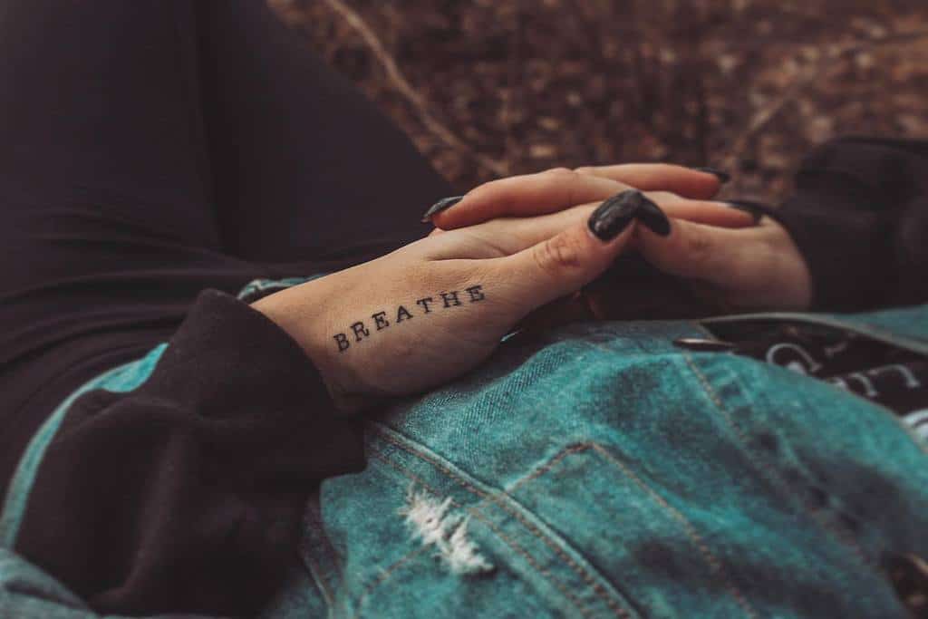 A close-up reveals a "BREATHE" tattoo gracefully inked on a hand