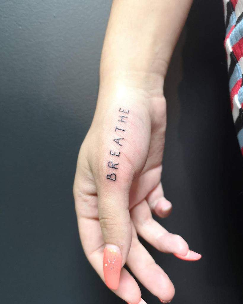 A hand adorned with the word "BREATHE" elegantly tattooed along the side of a finger