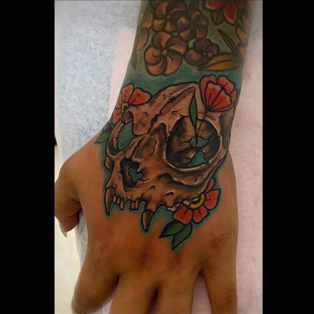 Hand tattoo featuring a cat skull with colorful flowers surrounding it