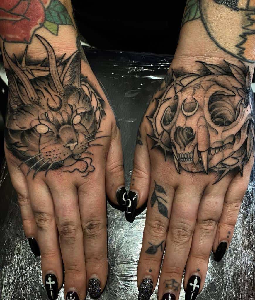 Hands with detailed tattoos of cat skulls, featuring moons and thorns on the fingers and nails