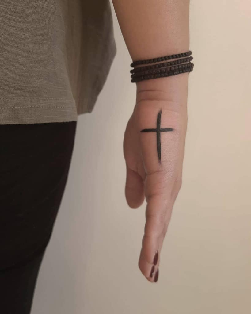 A hand adorned with a black cross tattoo on the side
