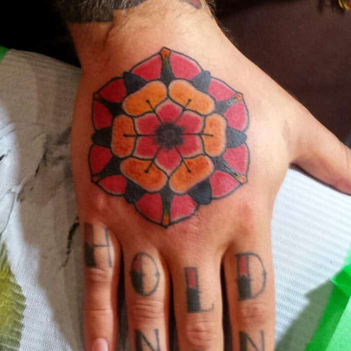 A hand tattoo featuring a red and black flower with the word "HOLD" inked on the fingers
