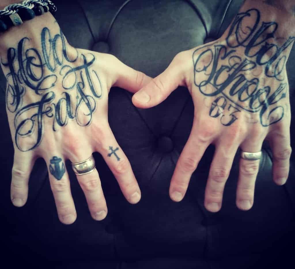 Hands with "Hold Fast" and "Old School 03" tattoos, rings, and a small cross tattoo