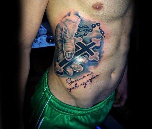 A man's torso with a tattoo of a hand holding a cross and text below it