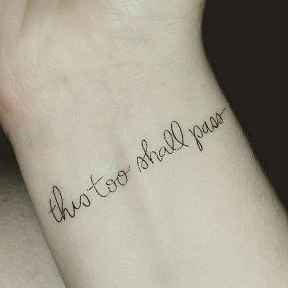 A "This Too Shall Pass" tattoo in cursive on a person's wrist.