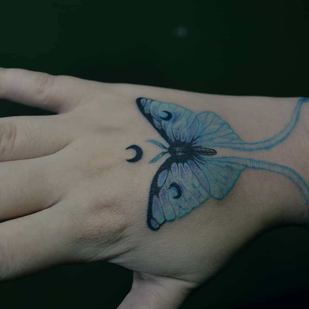 A colorful Luna Moth tattoo with blue and black detailing, accompanied by crescent moons near the wings