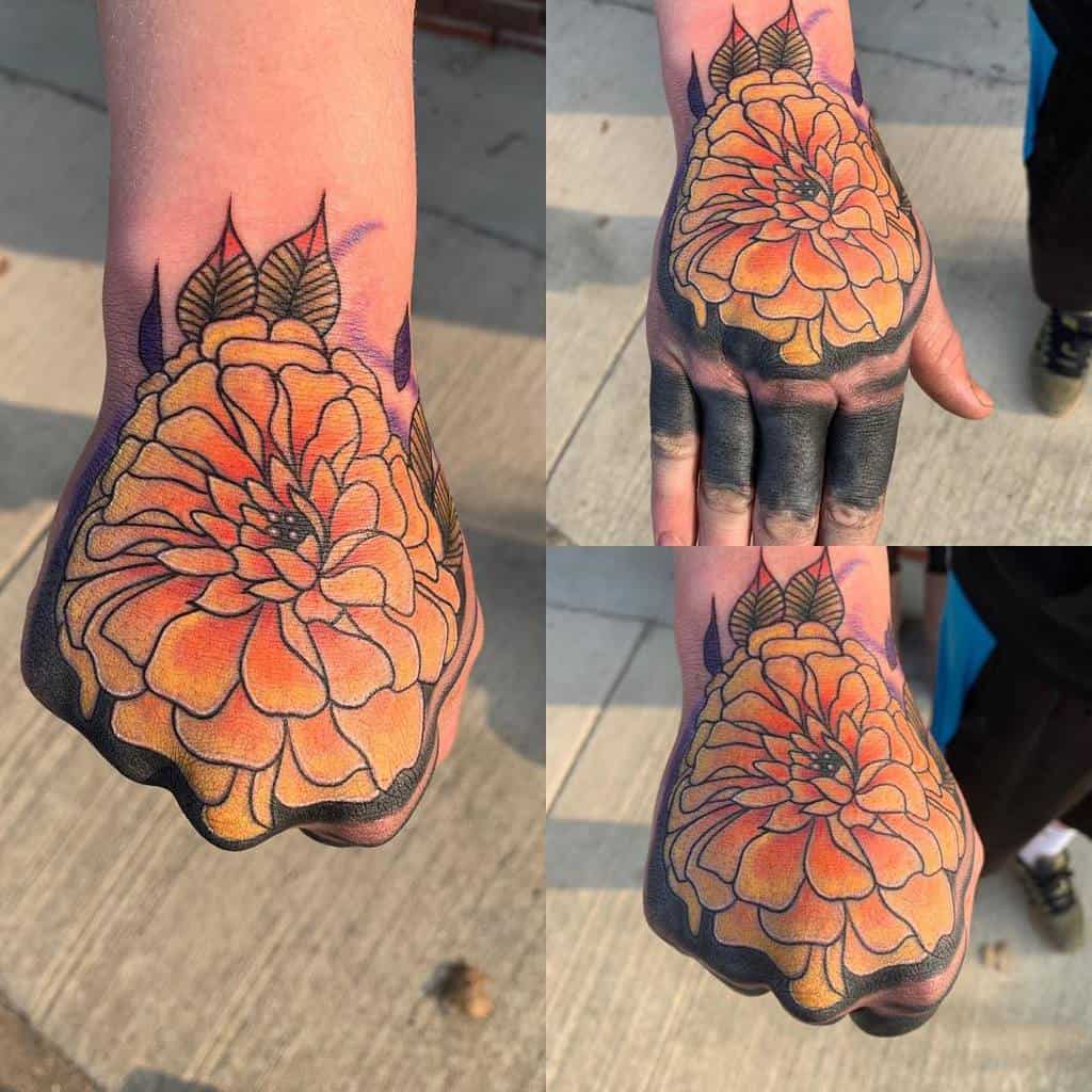 Bold tattoo featuring a large orange marigold with intricate shading, black ink accents, and a gradient fade