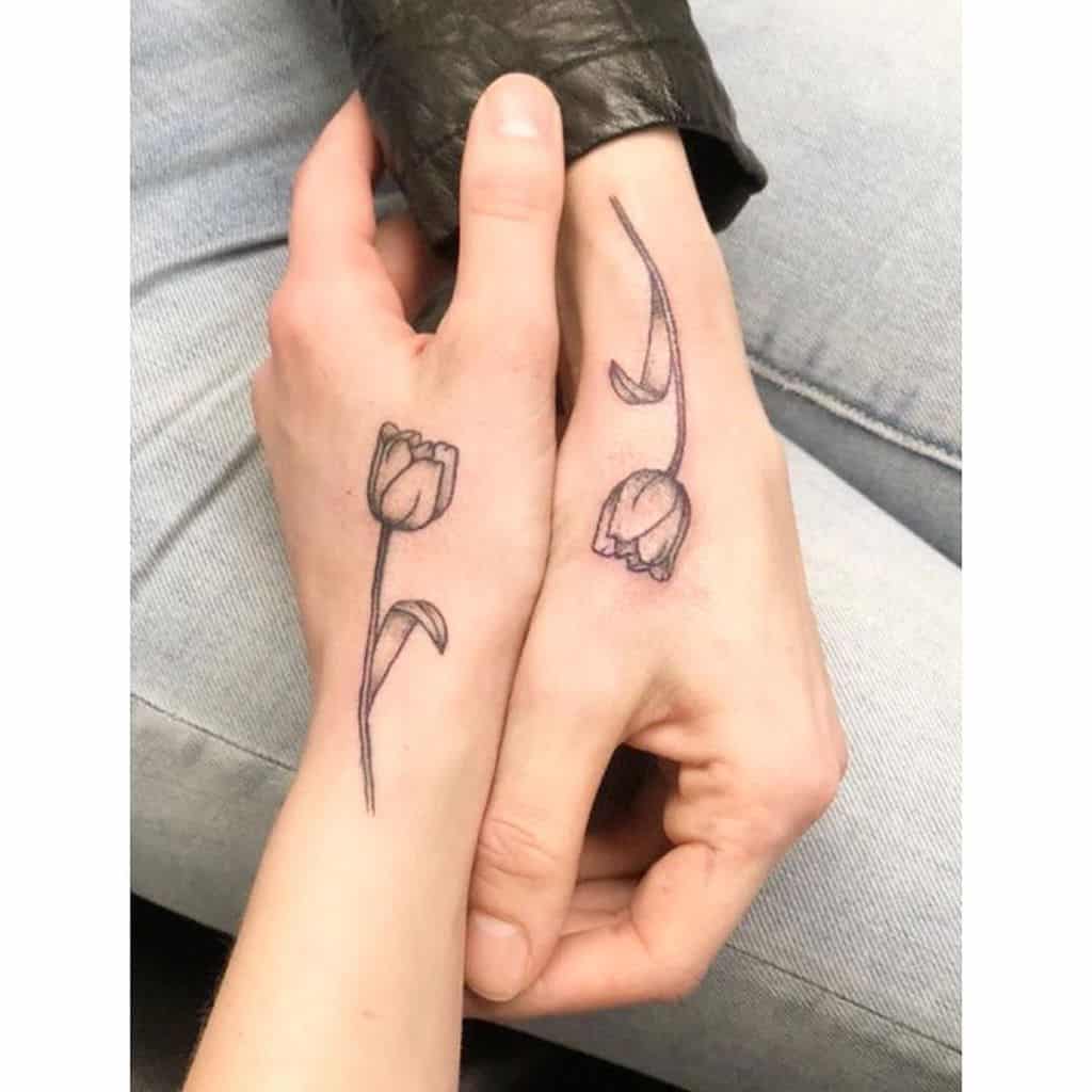 Matching tulip tattoos on two hands, featuring delicate flowers with long, curved stems and fine-line detailing.