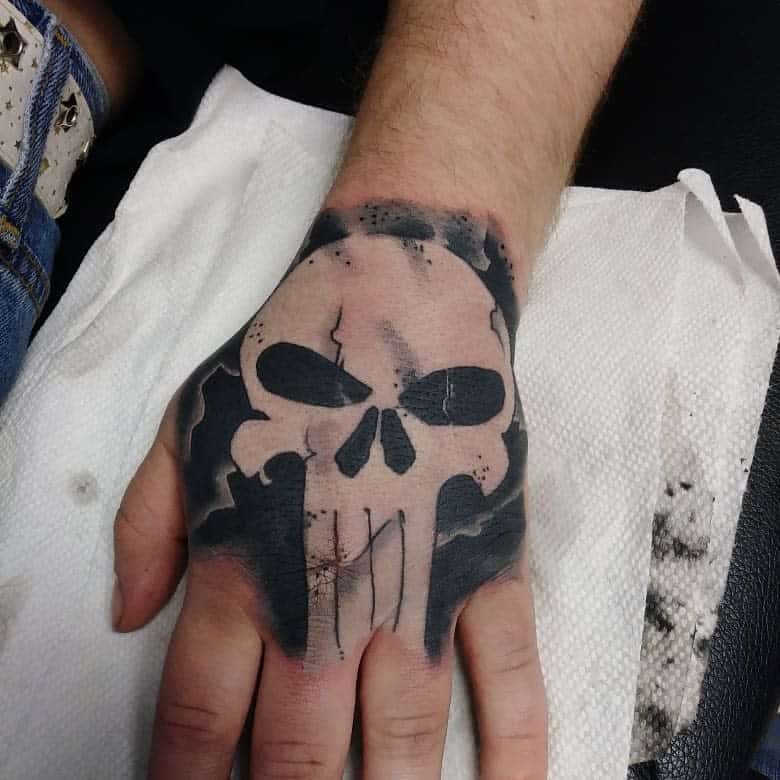 Punisher Skull tattoo on the hand, featuring a dark, cracked design with bold black shading, creating a rugged and intense look