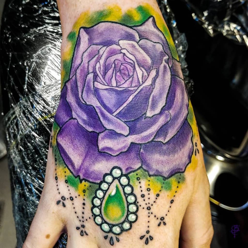 A striking hand tattoo showcases a vibrant purple rose, elegantly adorned with a teardrop-shaped jewel and intricate decorative dots