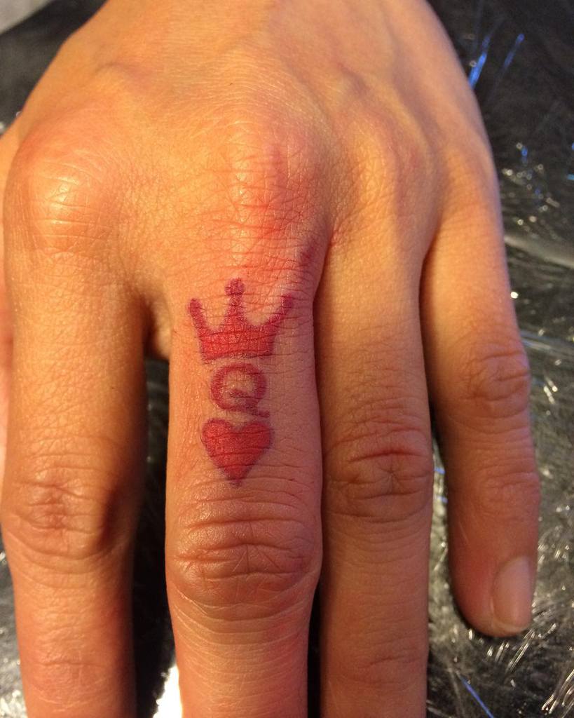 Hand with a red Queen of Hearts tattoo on the ring finger