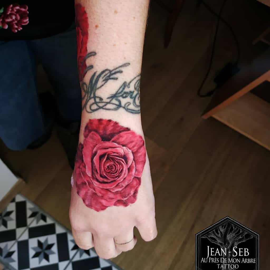 A realistic rose tattoo on a person's hand with script tattoo above