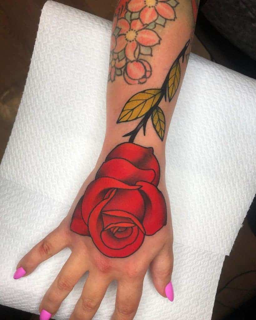 A hand with a red rose tattoo on the back and floral designs on the wrist