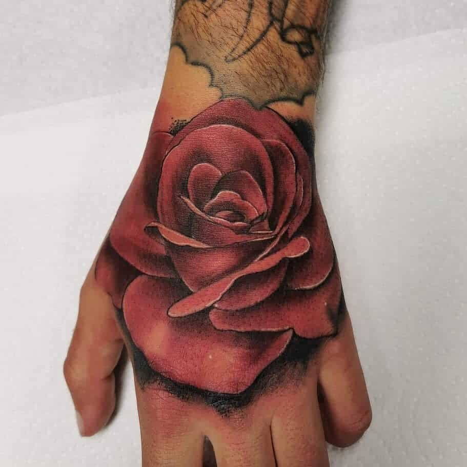 A vibrant red rose tattoo graces the back of a person's hand, adding a bold splash of color to their skin