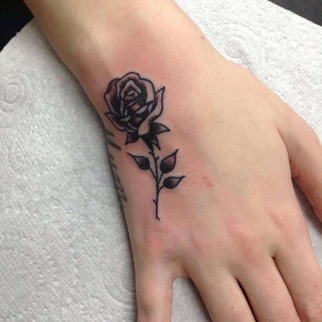 Black rose tattoo with a striking stem elegantly inked on the back of a hand
