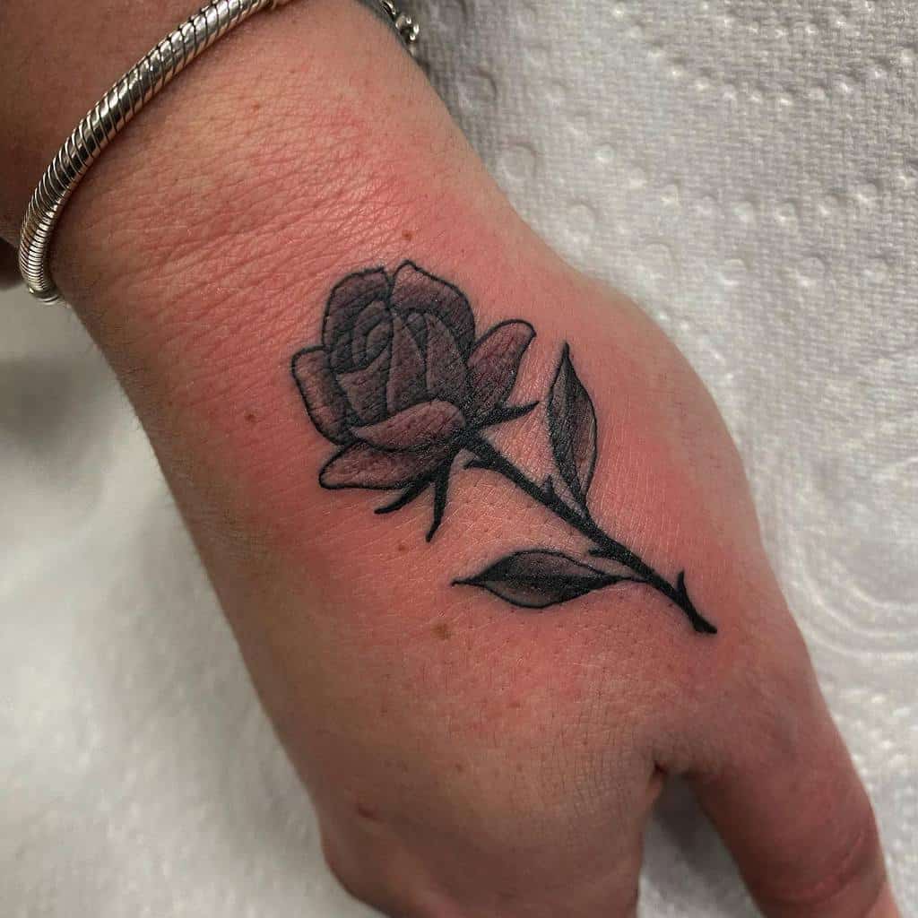 A black rose tattoo with an elegant stem winds along the hand