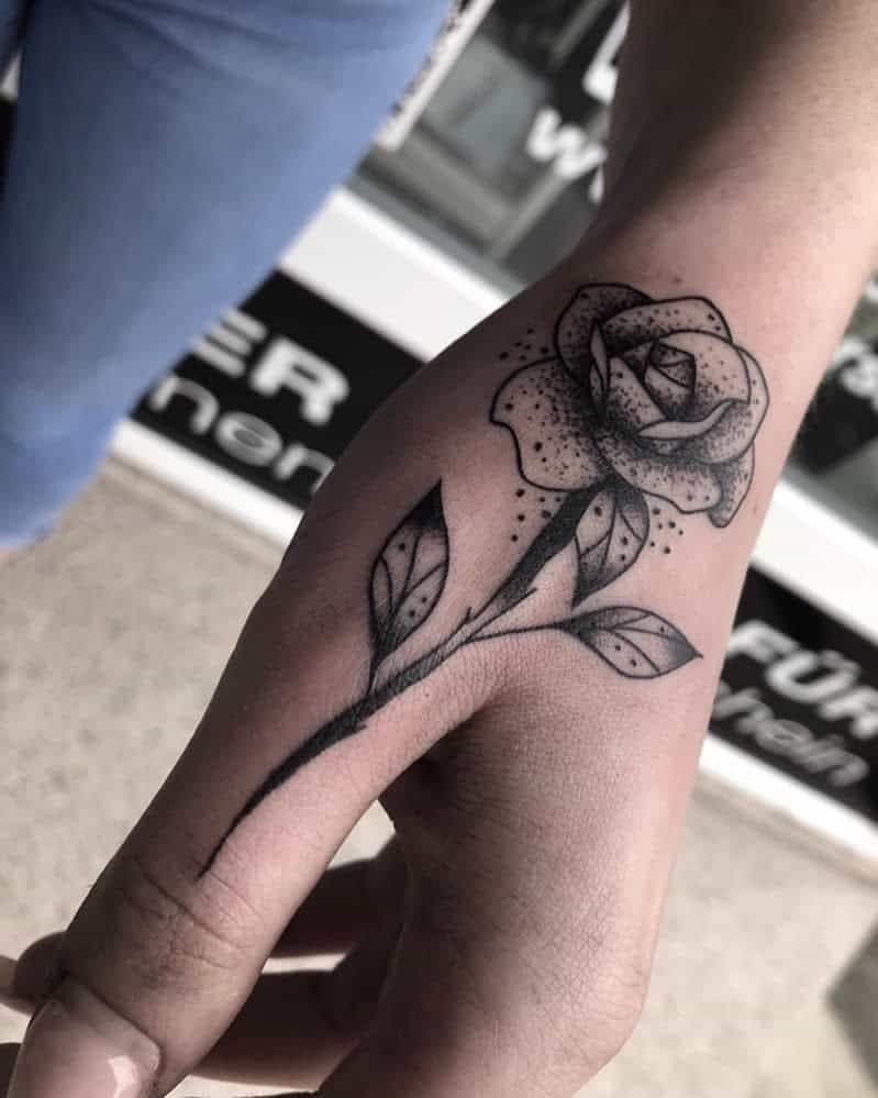 Black rose tattoo on a hand with leaves and small dots