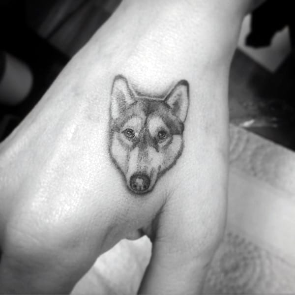 Small realistic Siberian Husky tattoo on the back of a hand, featuring fine details and soft shading for a subtle yet striking design.