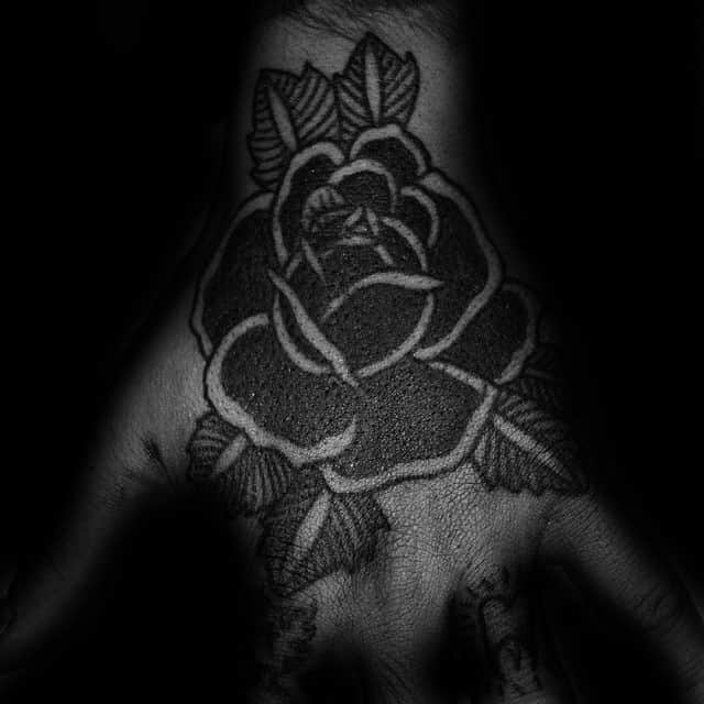 Black rose tattoo on a hand, with detailed shading and leaves