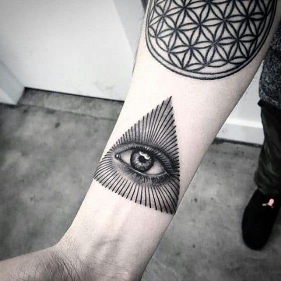 Forearm tattoo of an all-seeing eye inside a shaded triangle with radiating lines, inked in black with fine details.