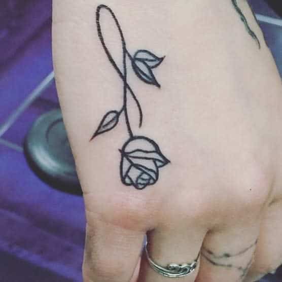A hand with a delicate rose tattoo on the side, featuring a simple line design of a rosebud and leaves