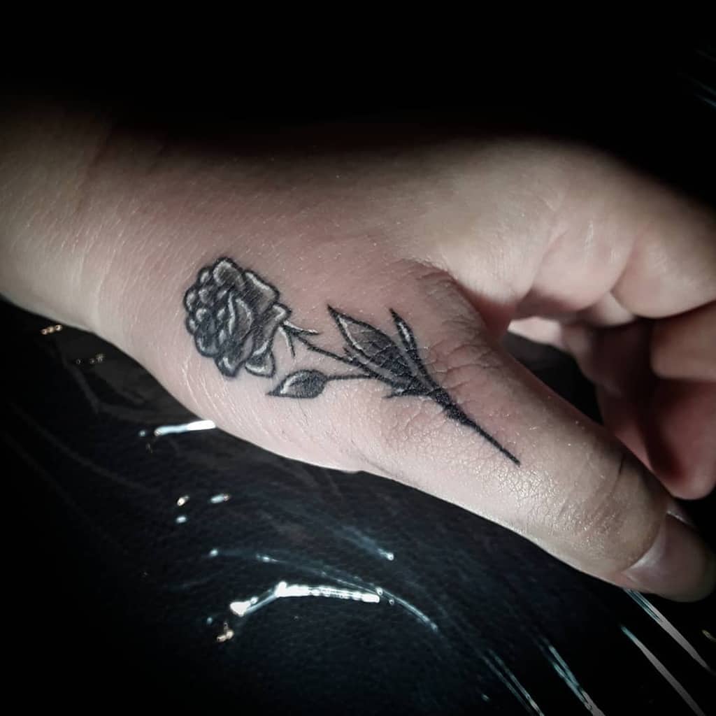 Black rose tattoo on a hand, positioned on the thumb