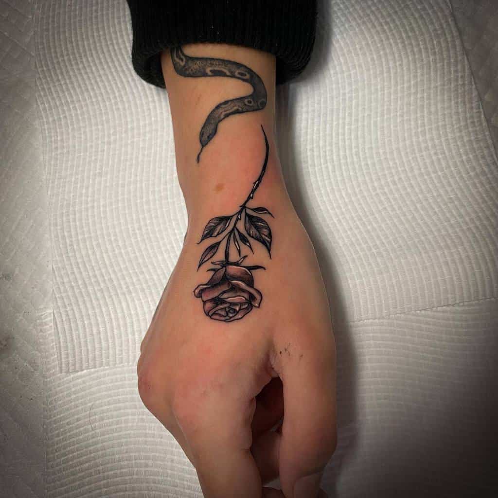 A hand with a tattoo of a rose on the wrist and a snake on the forearm