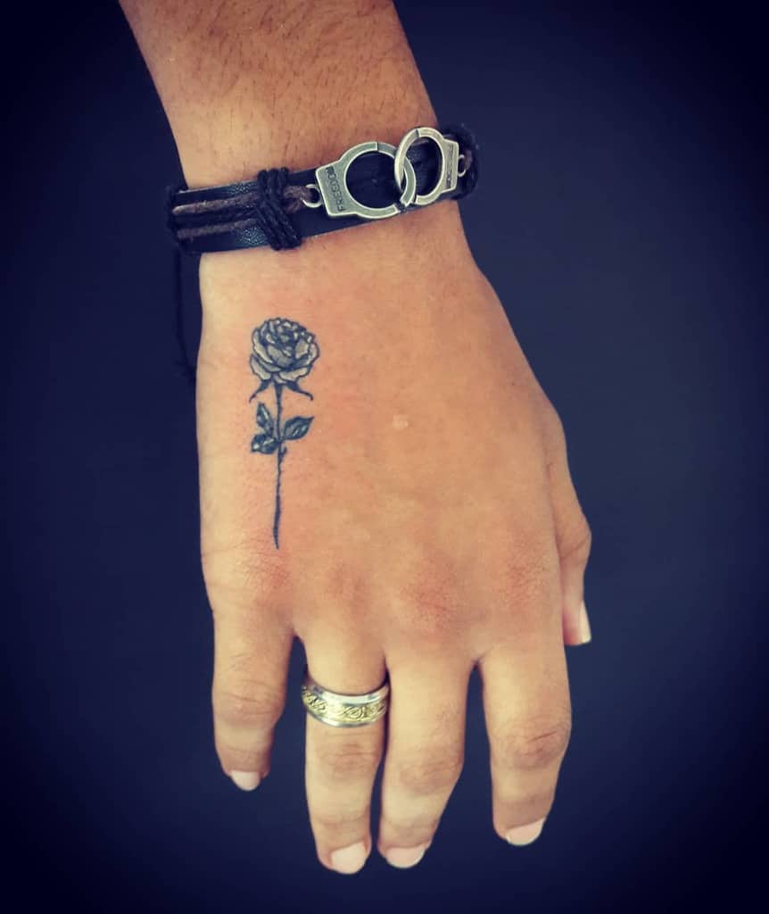 Small black rose tattoo on the hand, featuring fine-line details and delicate shading