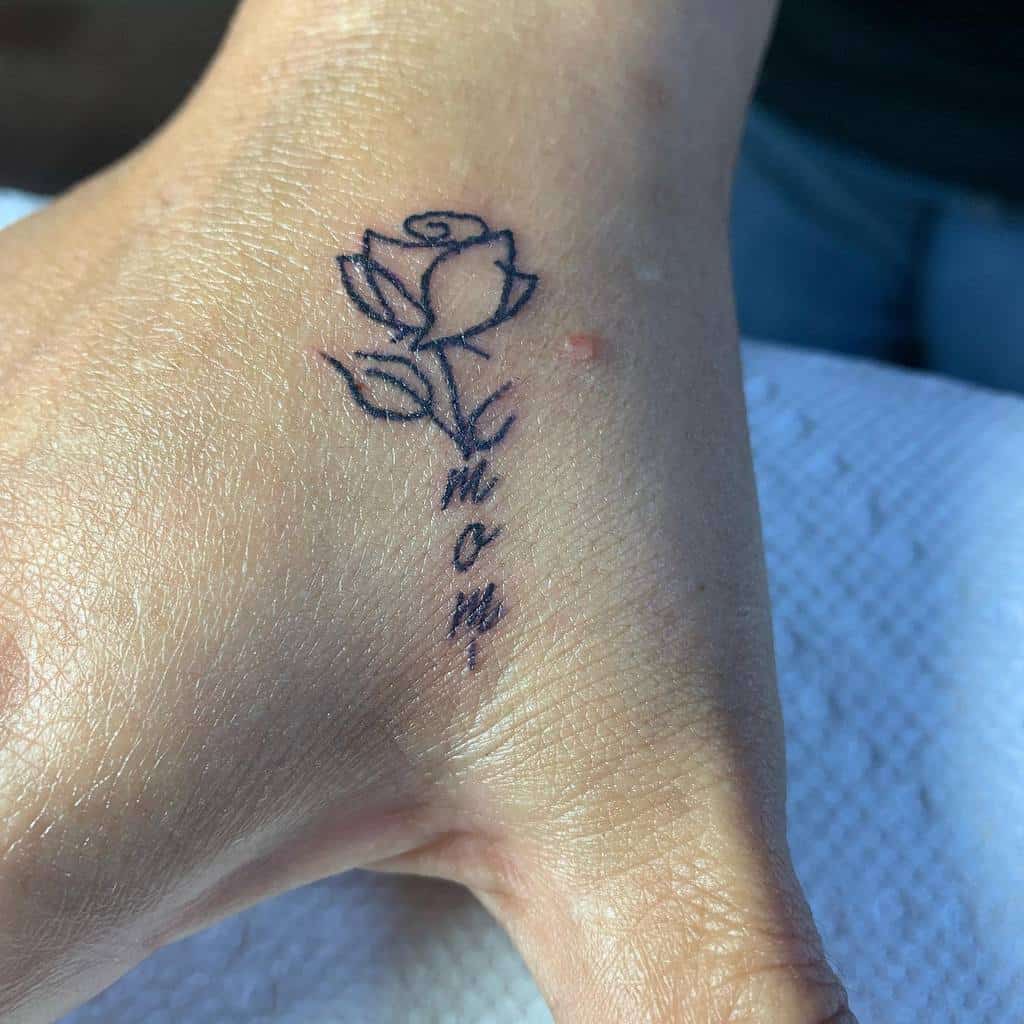 A small rose tattoo with the word "mom" on a person's hand