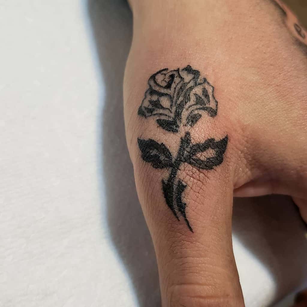 A tribal black rose tattoo elegantly adorns a person's thumb