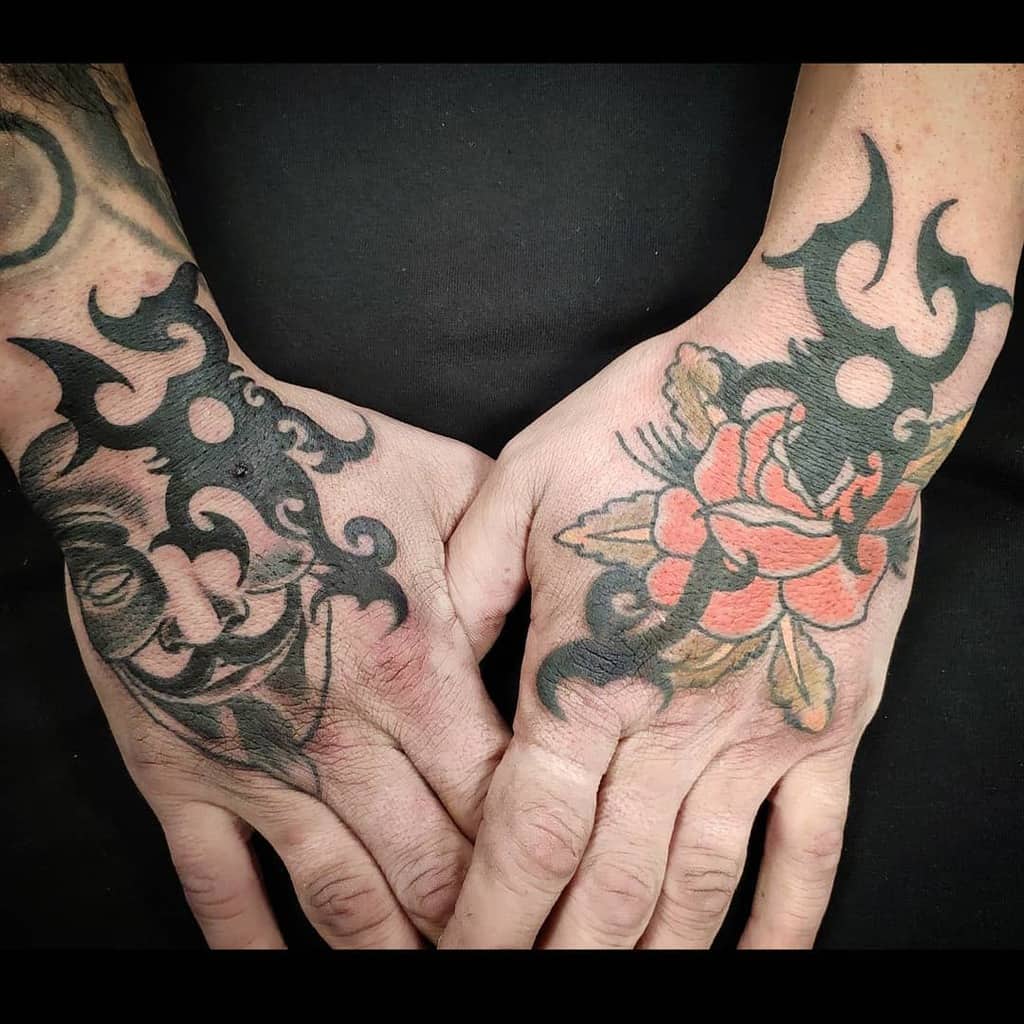A bold tattoo design on both hands, featuring intricate tribal patterns with one hand showcasing a detailed rose in vibrant red and green hues