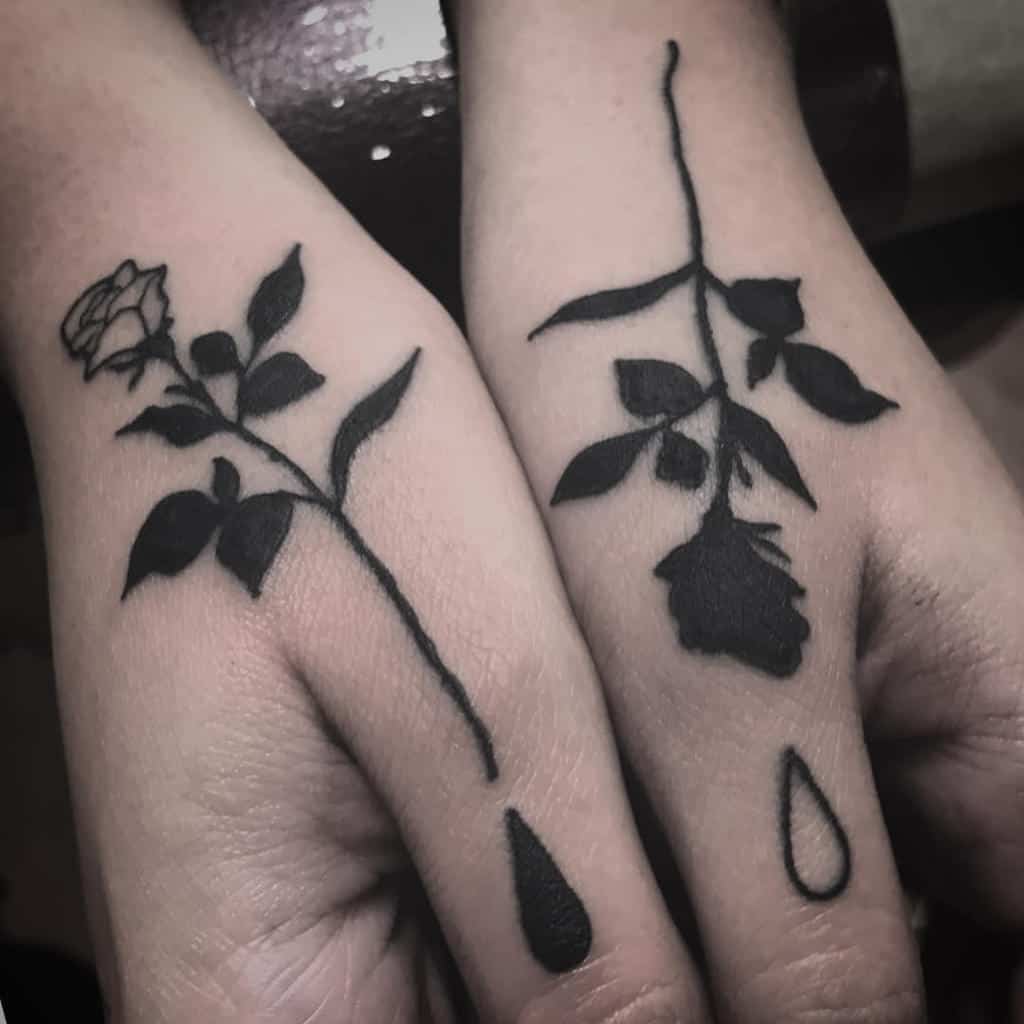Two hands adorned with tribal tattoos of a rose and leaves, each featuring a drop below