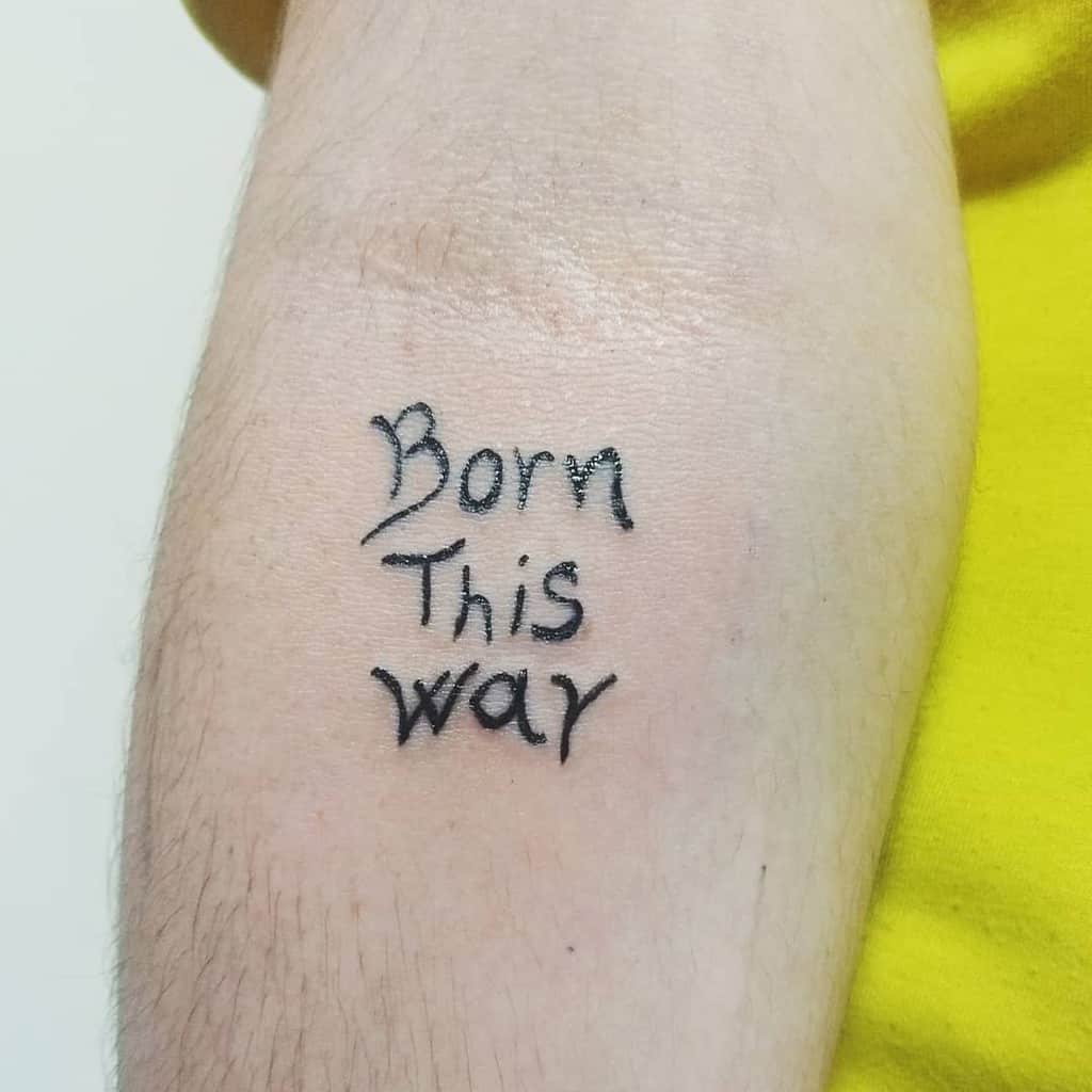 Tattoo on an arm reading "Born This Way" in stylized black lettering