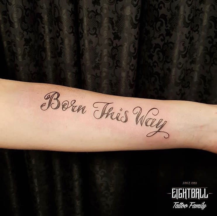 Forearm tattoo reading "Born This Way" in cursive script