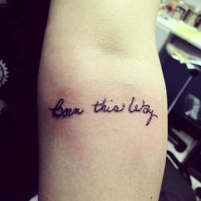 Tattoo on an arm reads "Born this way" in cursive script