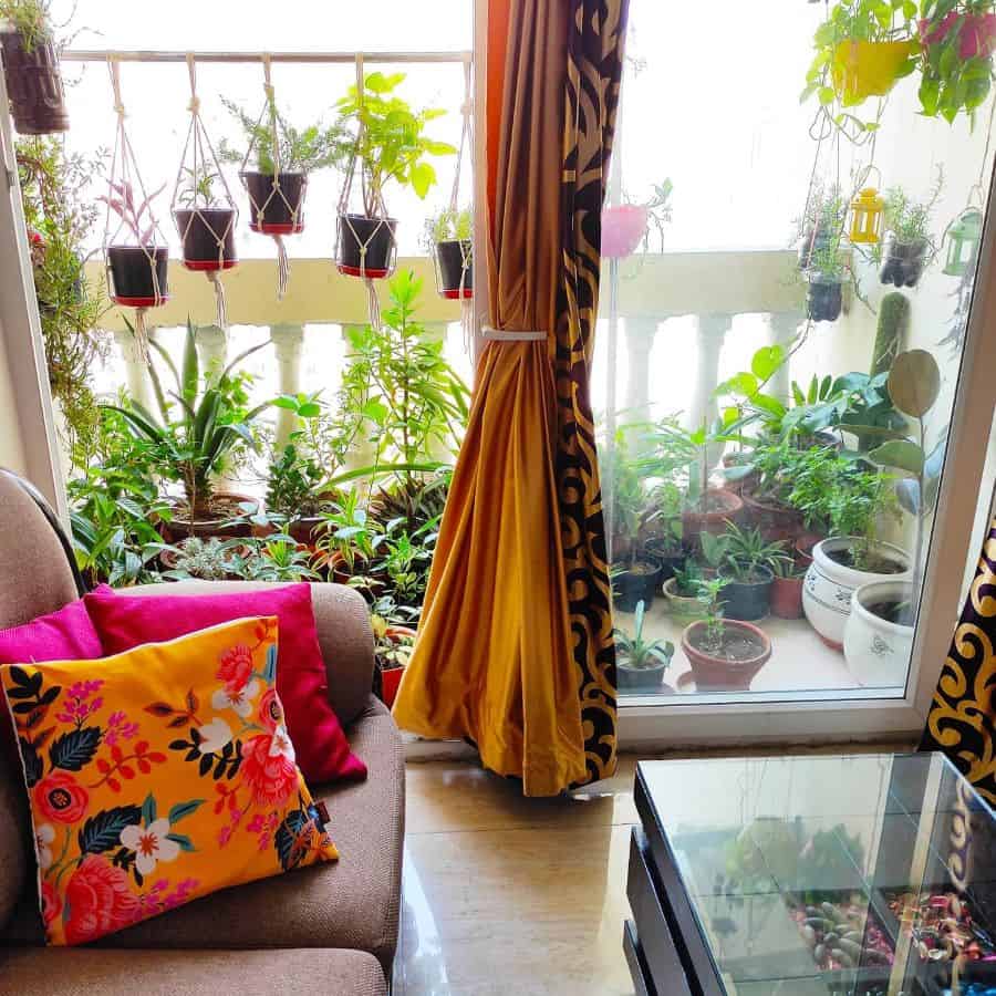Indoor seating area with a view of a balcony garden filled with potted and hanging plants.