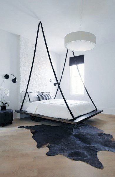 Modern bedroom with a hanging bed, black rope accents, and a black fur rug on wood flooring.