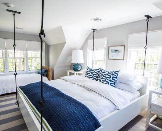 Bright bedroom with a hanging bed, nautical-themed bedding, and large windows for natural light.