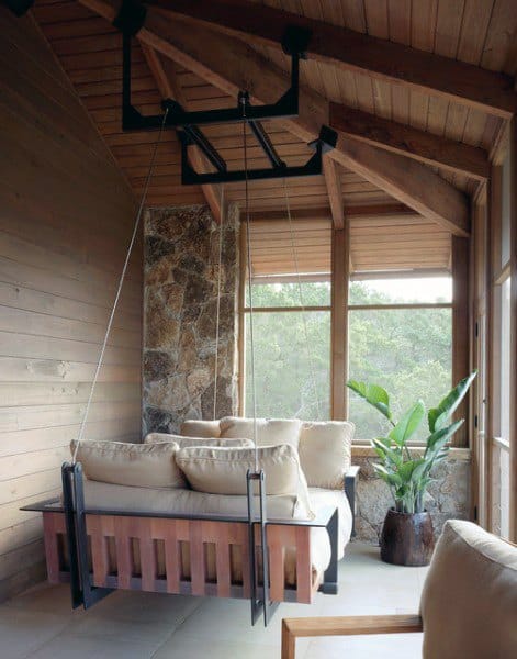 Wooden hanging daybed with cushions in a sunlit room featuring stone and wood accents.