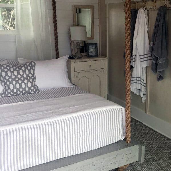 Cozy hanging bed with rope supports, striped bedding, and rustic decor in a serene bedroom.