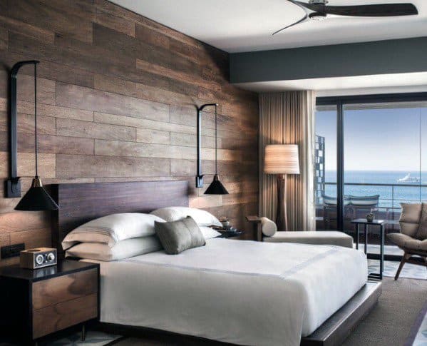 Modern bedroom with wood accent wall black wall sconces and ocean-view balcony.