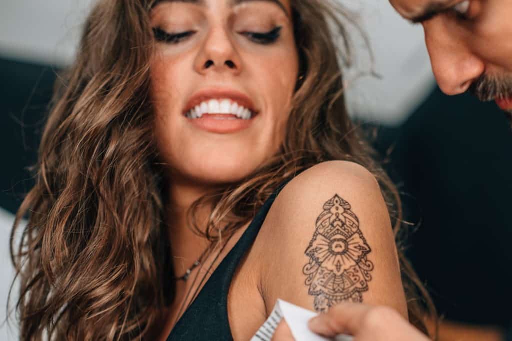 Happy Young Woman Gets Temporary Tattoo On Left Bicep