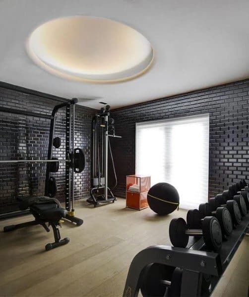 Home gym with black brick walls, light wood flooring, dumbbells, and modern workout equipment.