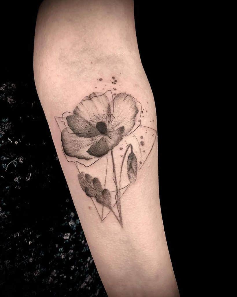 Delicate black ink tattoo featuring a floral design with fine linework, subtle shading, and a geometric Deathly Hallows symbol in the background.
