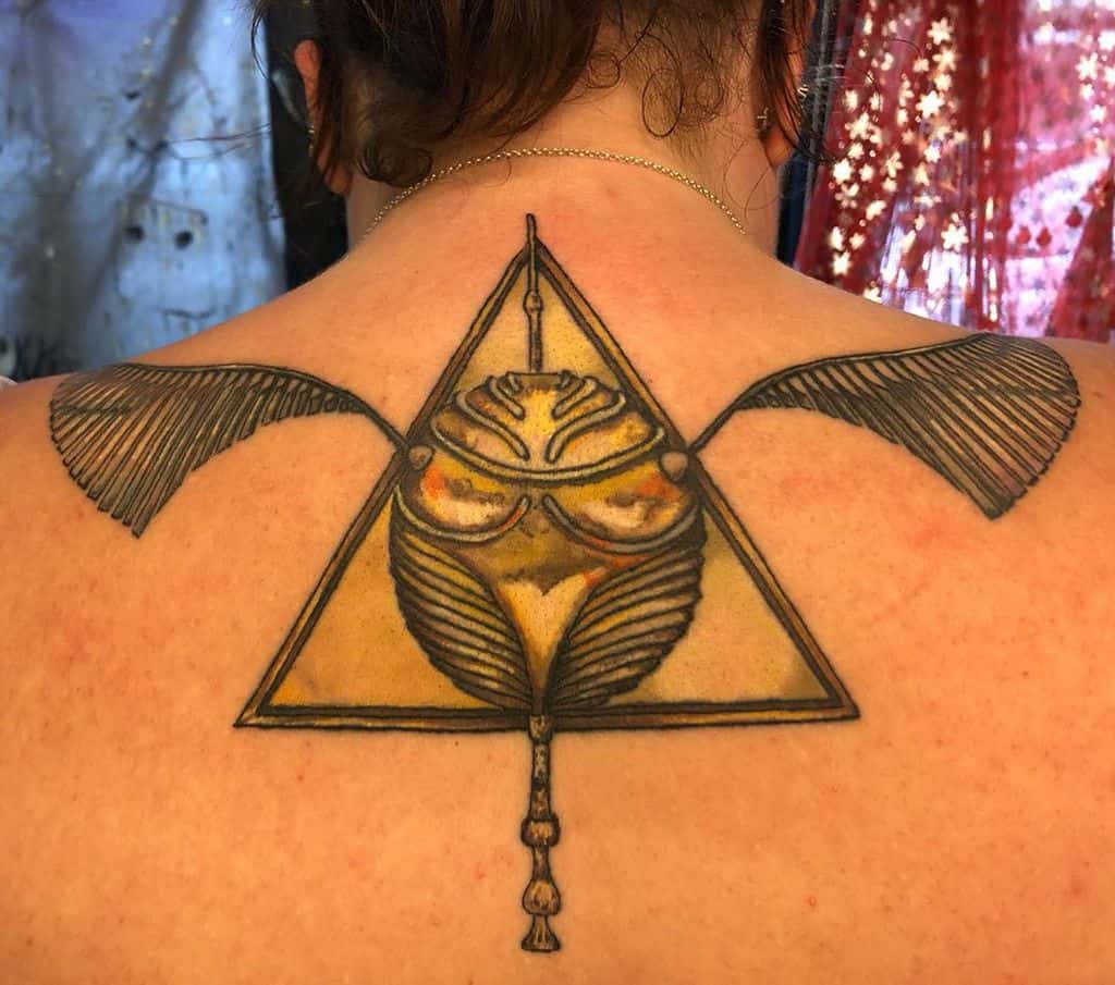 Large back tattoo featuring the Deathly Hallows symbol fused with a Golden Snitch, with outstretched wings and golden hues for a striking look.