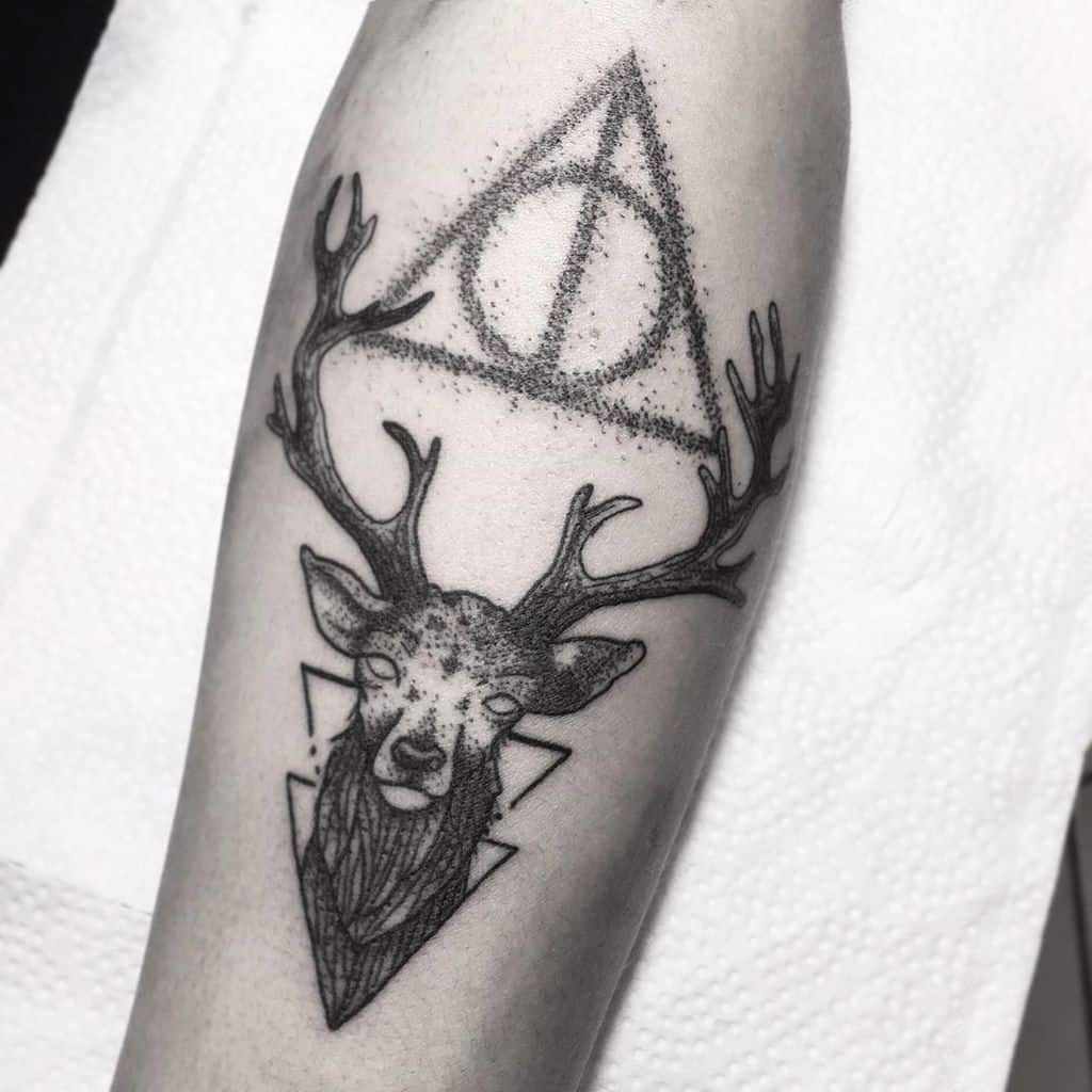 Black ink Deathly Hallows tattoo featuring a detailed stag with geometric elements, dotwork shading, and a mystical design.